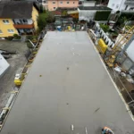 Ein Arbeiter glättet frischen Beton auf einem großen Gebäudefundament auf einer Wohnbaustelle.